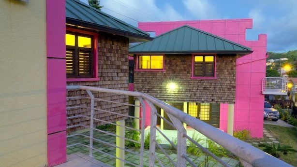 A modern building with pink and yellow exterior walls, a green roof, and a visible staircase leading to a balcony.