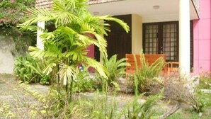 A house with a tiled roof, a porch with a bench, and various plants in the yard.