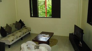 A living room with a sofa, a coffee table, a TV stand, and a window with shutters.