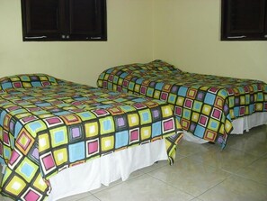 Dos camas individuales con ropa de cama de diseños geométricos coloridos en una habitación con suelo de baldosas y paredes lisas.