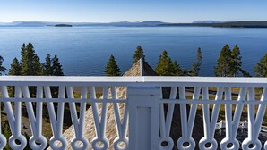 A balcony with a white railing overlooking a calm lake with distant mountains.
