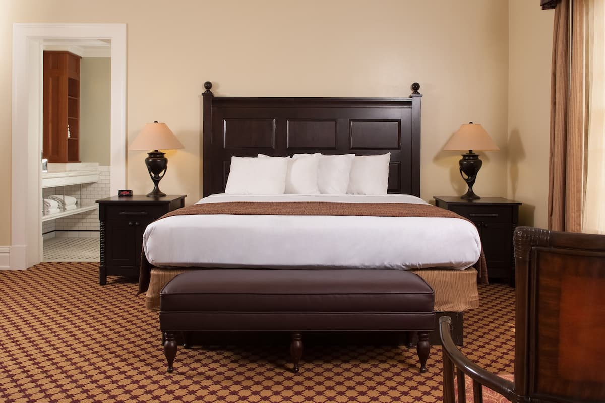 A neatly made bed with white linens, two bedside tables with lamps, a wooden headboard, and a patterned carpet.