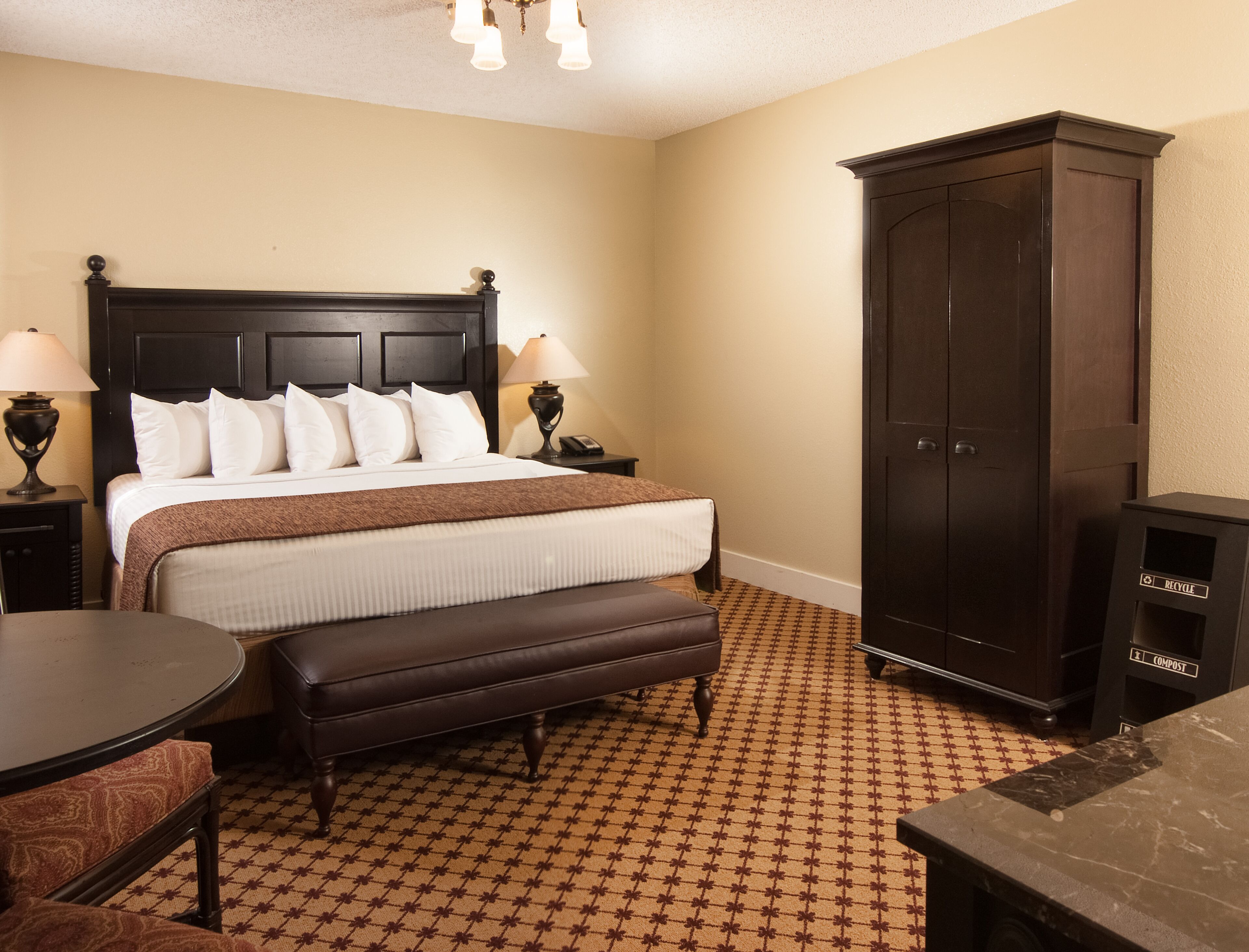 Une chambre d’hôtel avec un grand lit, deux tables de chevet avec des lampes, une armoire en bois foncé, un banc et une petite table.