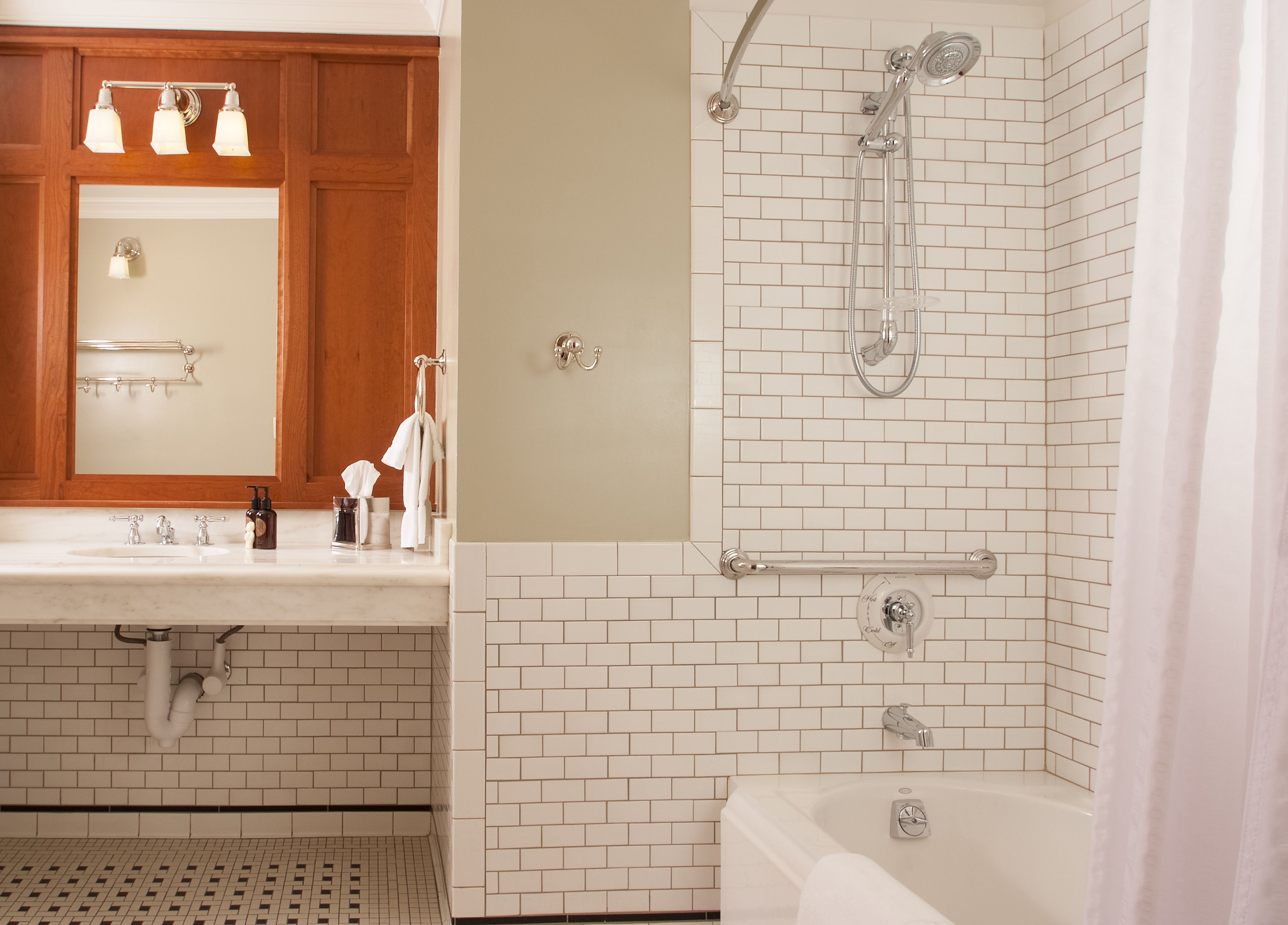 A bathroom with a white-tiled shower, a sink with a mirror, and a towel rack.
