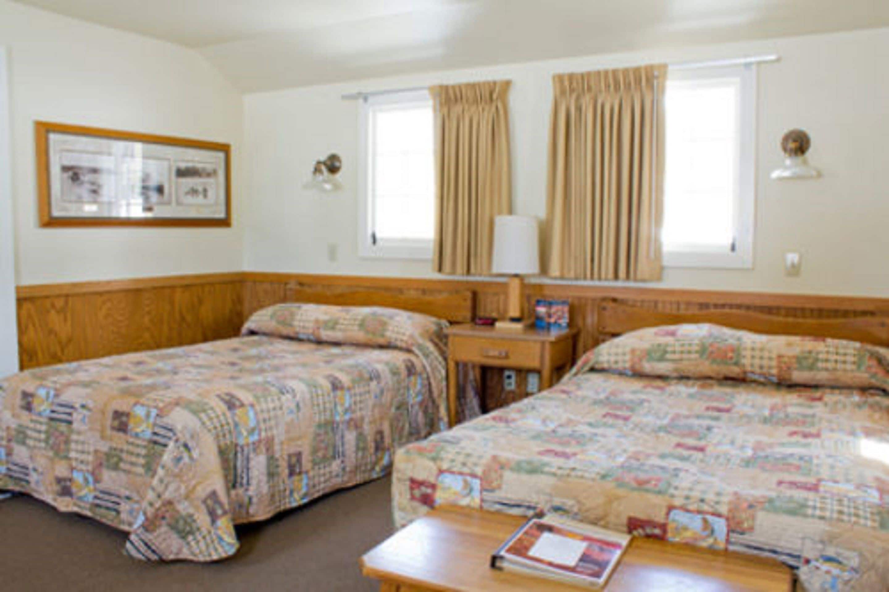 A room with two beds, a nightstand, a lamp, and a framed picture on the wall.