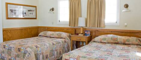 A room with two beds, a nightstand, a lamp, and a framed picture on the wall.