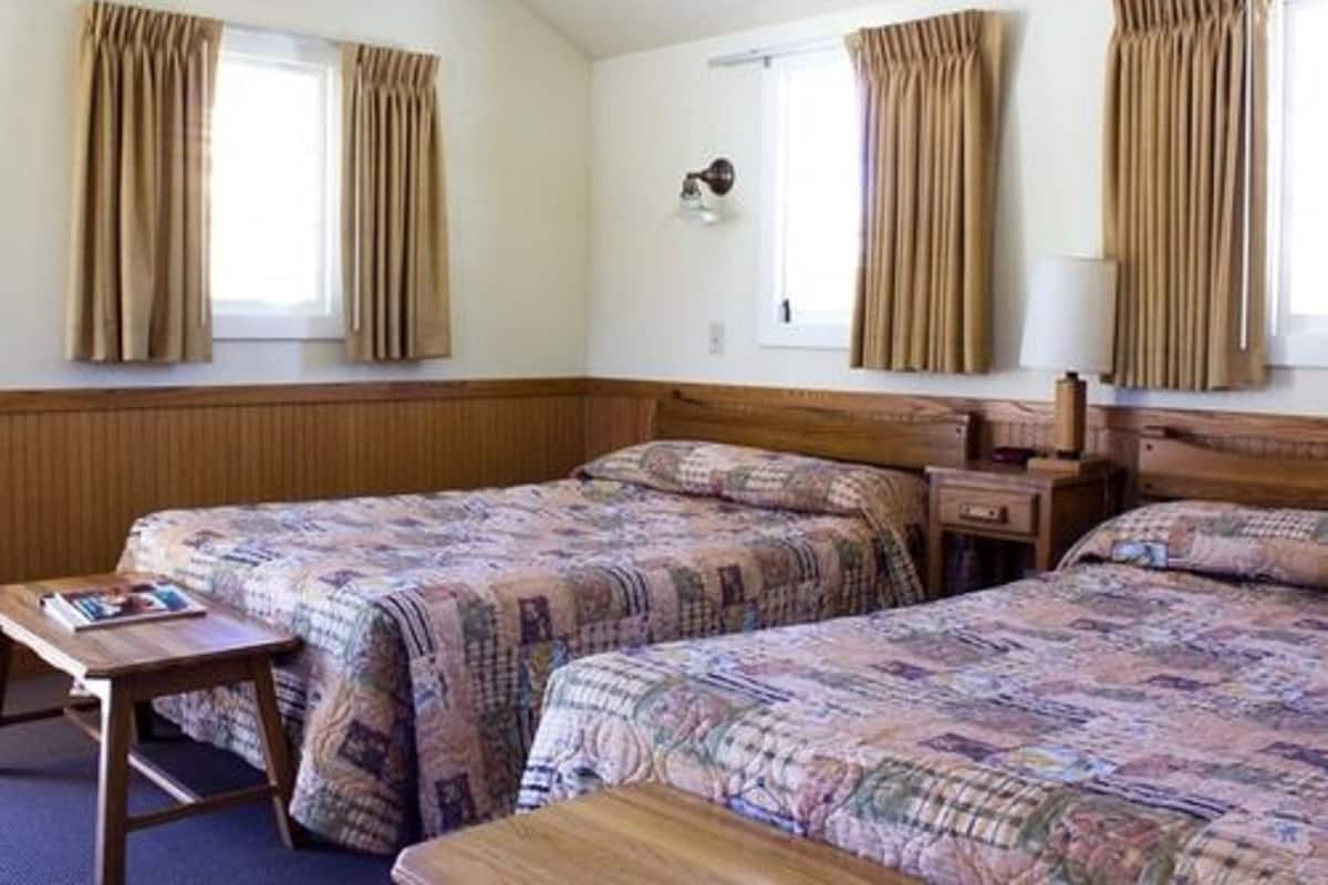 A hotel room with two beds, a wooden headboard, a bedside table, and a lamp.