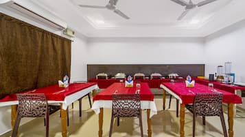 A conference room with tables covered in red tablecloths, wooden chairs, and ceiling fans.
