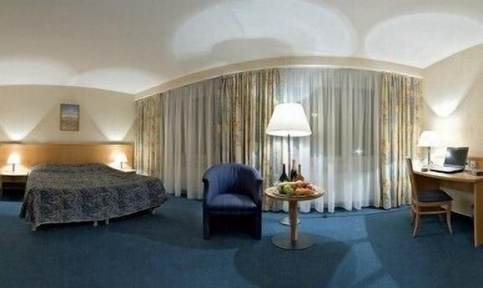 Une chambre d’hôtel avec un lit, un bureau, une chaise, une lampe et une petite table sur laquelle se trouvent des fruits.
