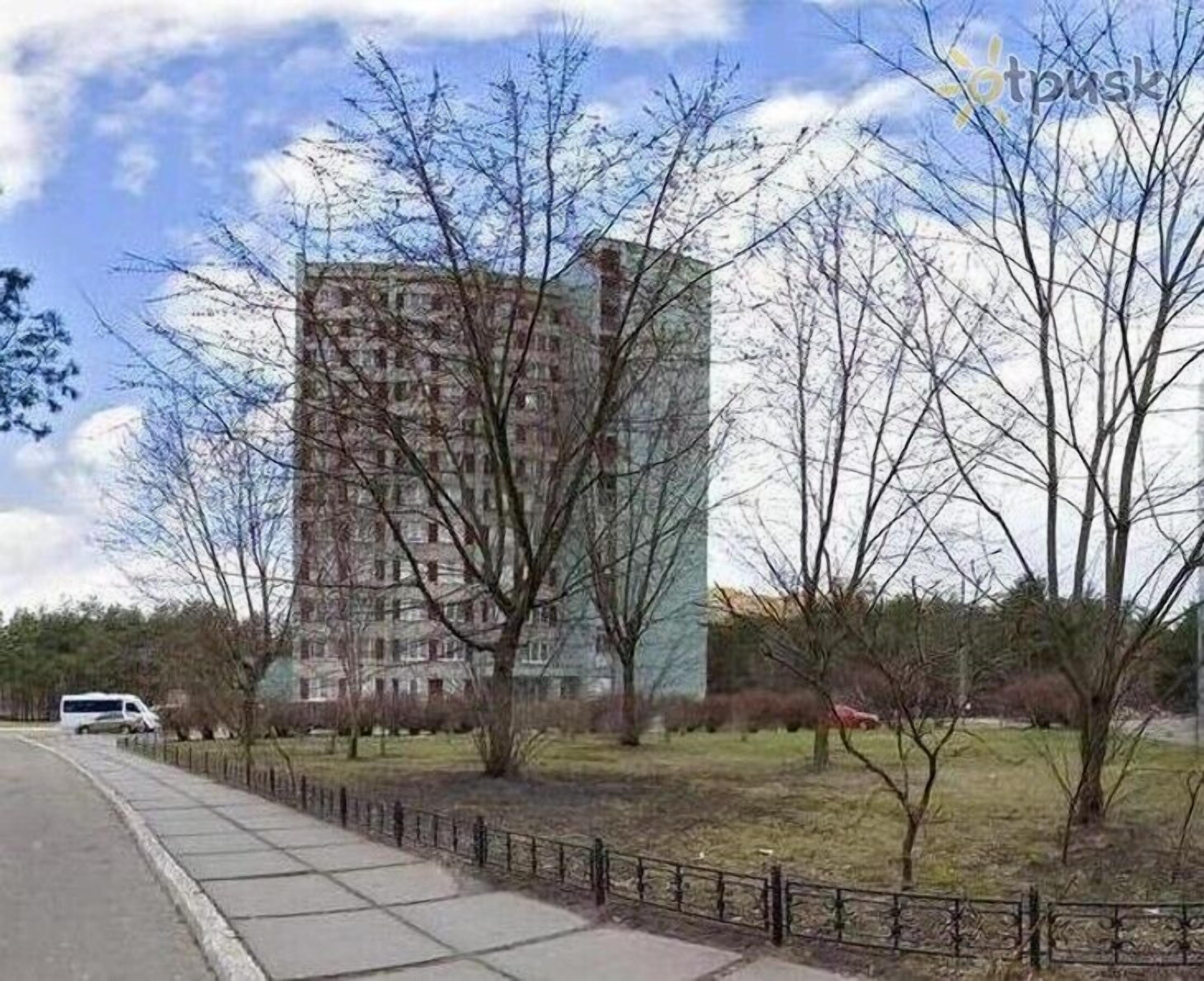 Un immeuble résidentiel de grande hauteur, doté d’une architecture moderne, entouré d’un espace verdoyant avec des arbres et d’un chemin piétonnier dallé.