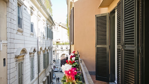 Una calle estrecha flanqueada por edificios, un balcón adornado con flores y un camino empedrado.