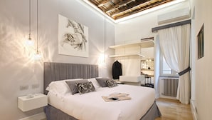 Un dormitorio moderno con una cama grande, mesitas de noche, una lámpara colgante, un ventilador de techo y una ventana con cortinas.