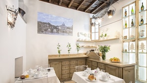 Un comedor con mesas dispuestas para el servicio de té, una encimera de cocina con productos frescos y una vitrina de vinos.