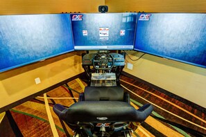 A racing simulator setup with a steering wheel and pedals, a large screen displaying racing graphics, and a carpeted floor. - Best Western Plus Drayton Valley (Drayton Valley)