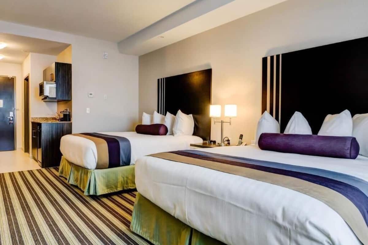 A hotel room with two beds, a kitchenette, a headboard with vertical lines, and a striped carpet.
