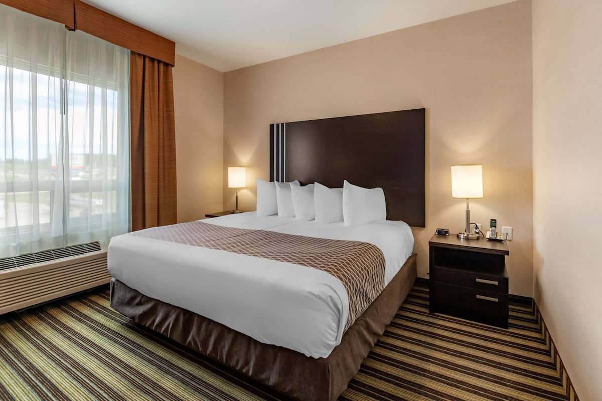 A hotel room with a large bed, two bedside lamps, a nightstand with a phone, and a window with curtains.