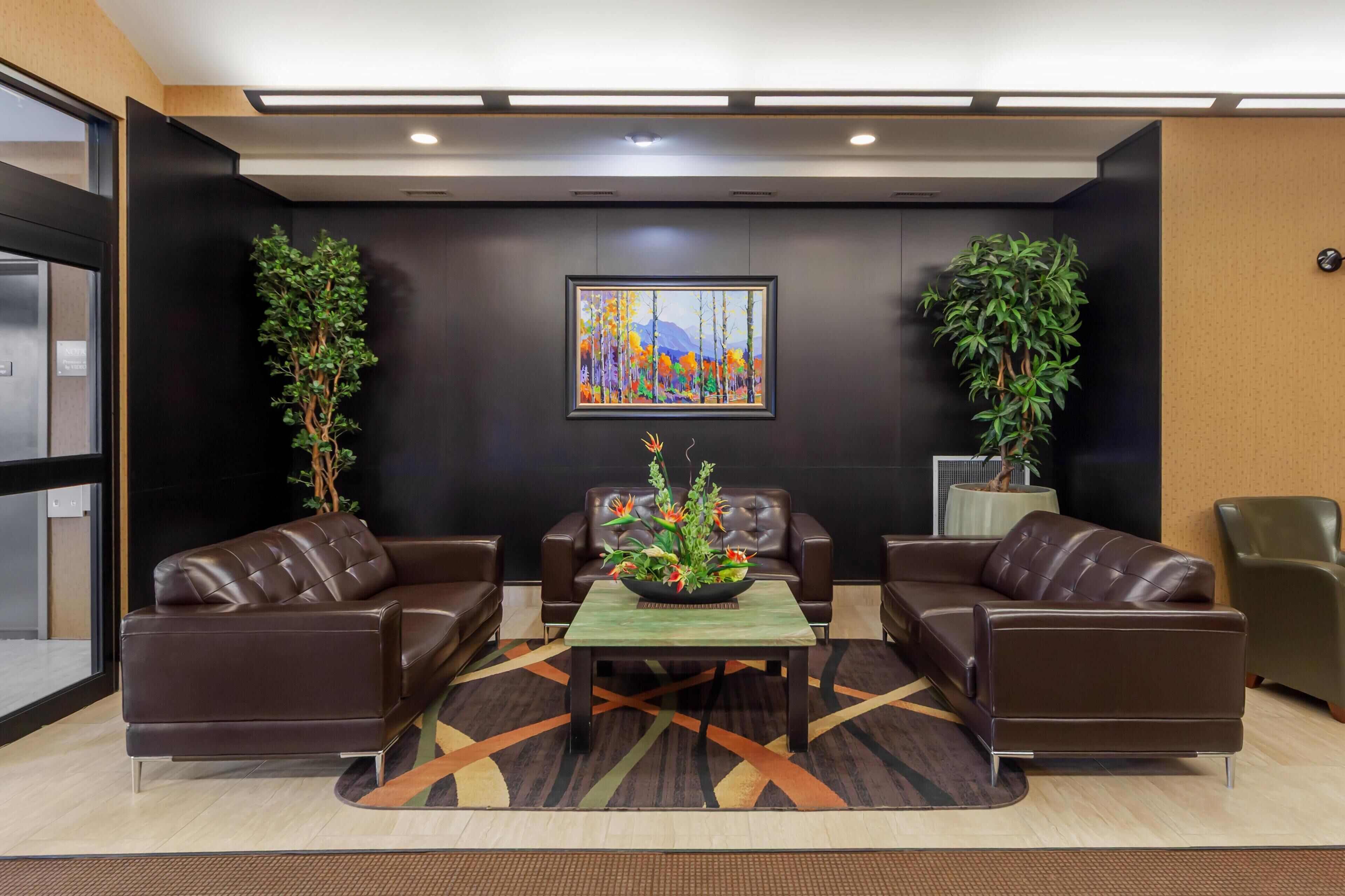 A lobby with leather sofas, a central table with a floral arrangement, and a painting on the wall.