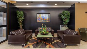 A lobby with leather sofas, a central table with a floral arrangement, and a painting on the wall.