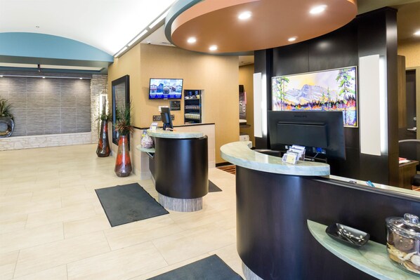A reception area with a modern design, featuring a reception desk, a flat-screen TV, and a large window with a cityscape view. - Best Western Plus Drayton Valley (Drayton Valley)