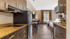 Cuina d'hotel senzilla amb vitroceràmica, nevera i microones integrades. Zona de dinar amb taula i cadires, i dormitori separat amb llit i finestra.