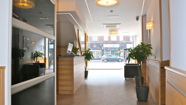 A modern hotel lobby with a reception desk, seating area, and potted plants. - London Kings Hotel (London)