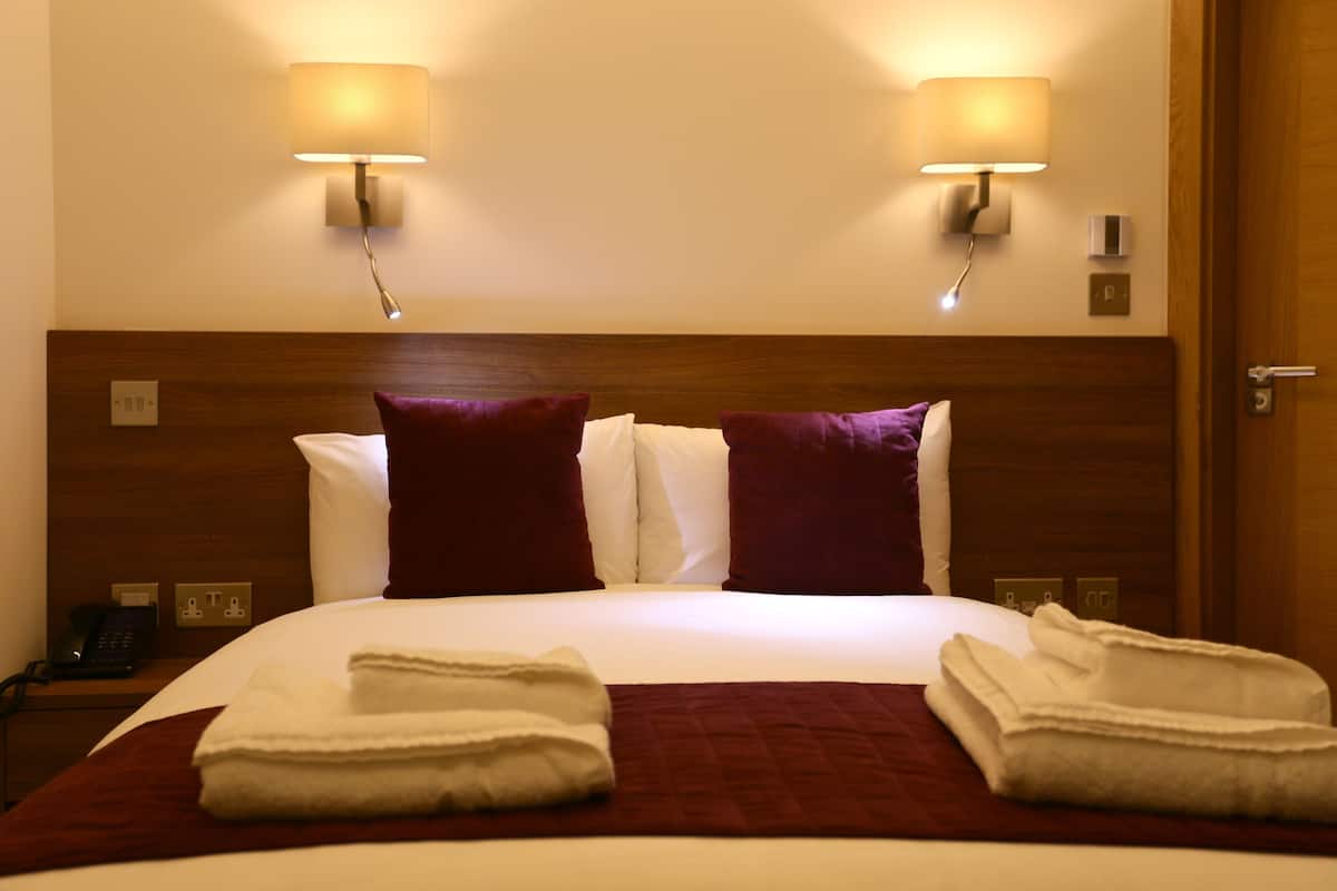A hotel room with a large bed, two wall-mounted lamps, a wooden headboard, and a telephone on a nightstand.