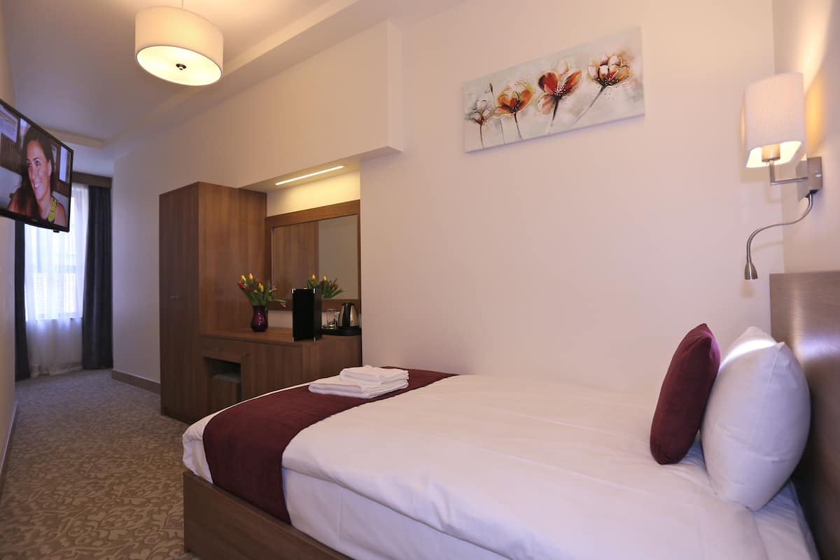 A hotel room with a bed, a desk, a mirror, and a painting on the wall.