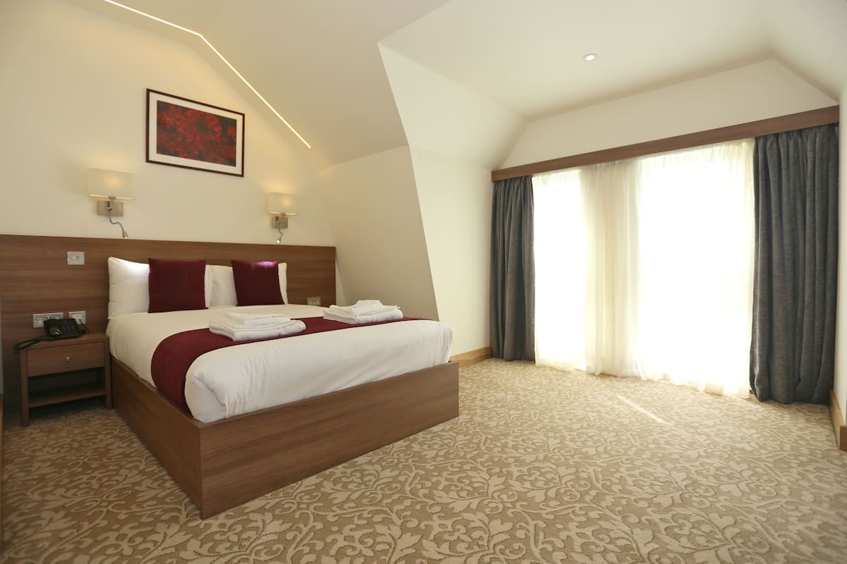 A hotel room with a large bed, a nightstand, a wall-mounted lamp, and a window with curtains.