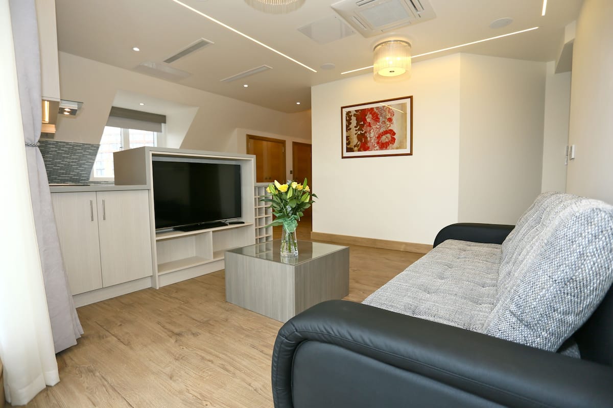 A modern living room with a black leather sofa, a glass coffee table, a flat-screen TV, and a decorative vase.