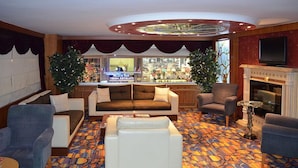 Eine Hotellobby mit einem gemusterten Teppich, Sofas, Sesseln, einem Kamin, einem Fernseher und einer Bar mit einem Schild.