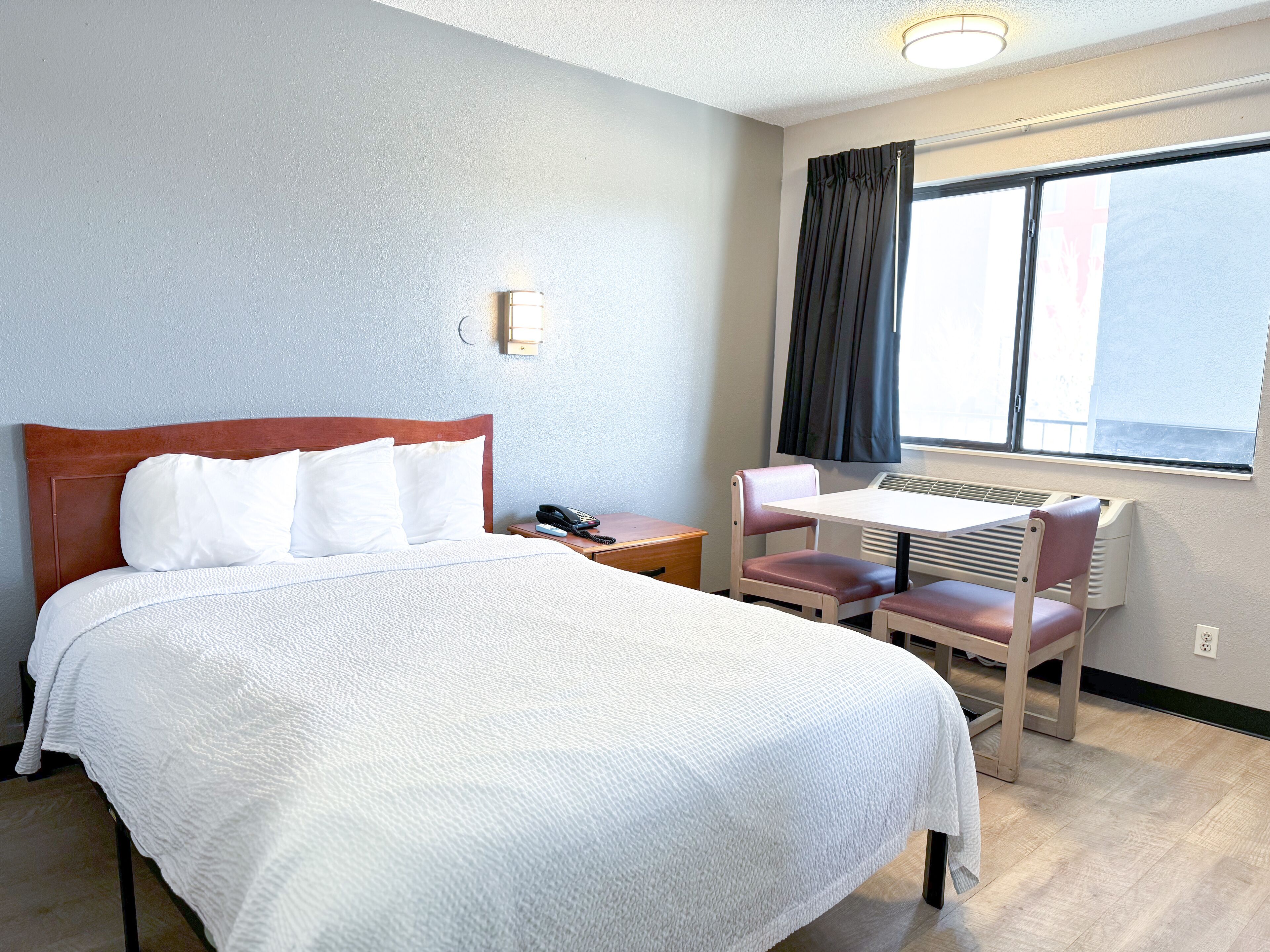 Une chambre d’hôtel équipée d’un lit, d’un bureau, d’une chaise, d’un téléphone et d’une fenêtre avec des rideaux.