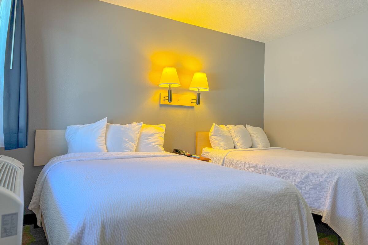 A hotel room with two beds, a wall-mounted lamp, and a ceiling fan.