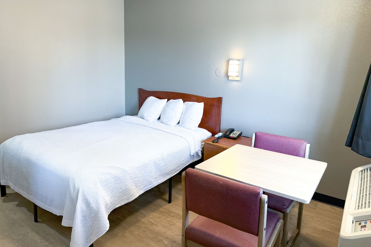 A hotel room with a bed, a bedside table with a phone, a chair, and a table.
