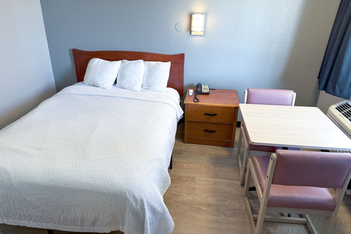 A hotel room with a bed, bedside table, desk, and chair.