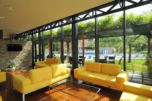 Ein modernes Wohnzimmer mit gelben Sofas, einer Steinwand und großen Fenstern mit Blick auf einen Pool und Garten.