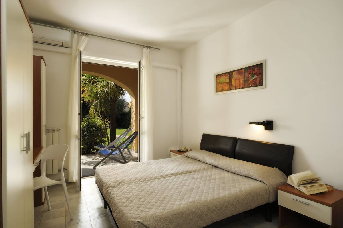 A bedroom with a bed, bedside table, chair, and a view of the outdoors.