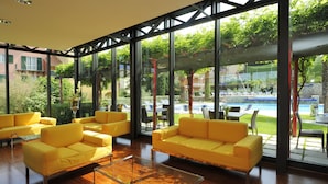 A modern indoor space with large windows, yellow sofas, and a view of an outdoor pool area. - Residence i Cormorani (Loano)
