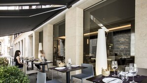 An outdoor dining area with tables set for two, featuring a modern design with dark tables and light chairs. - Vincci Mercat Hotel (Valencia)