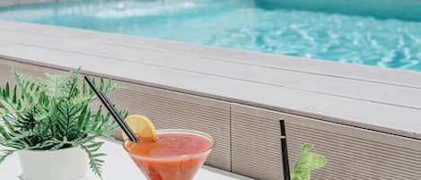 A poolside setting with a clear view of a swimming pool, a potted plant, and two drinks on a table.