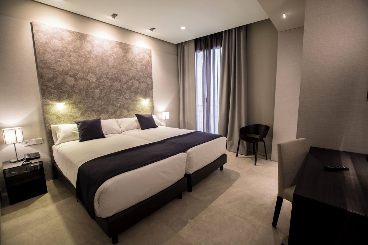 Quarto de hotel moderno com uma cama grande, mesas de cabeceira, uma escrivaninha e uma cadeira.