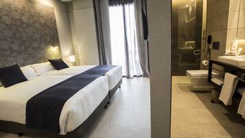 Habitación de hotel con una cama grande, baño separado con ducha de vidrio y diseño moderno.