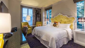A hotel room with a large bed, a desk with a computer, a chair, and a window with curtains.