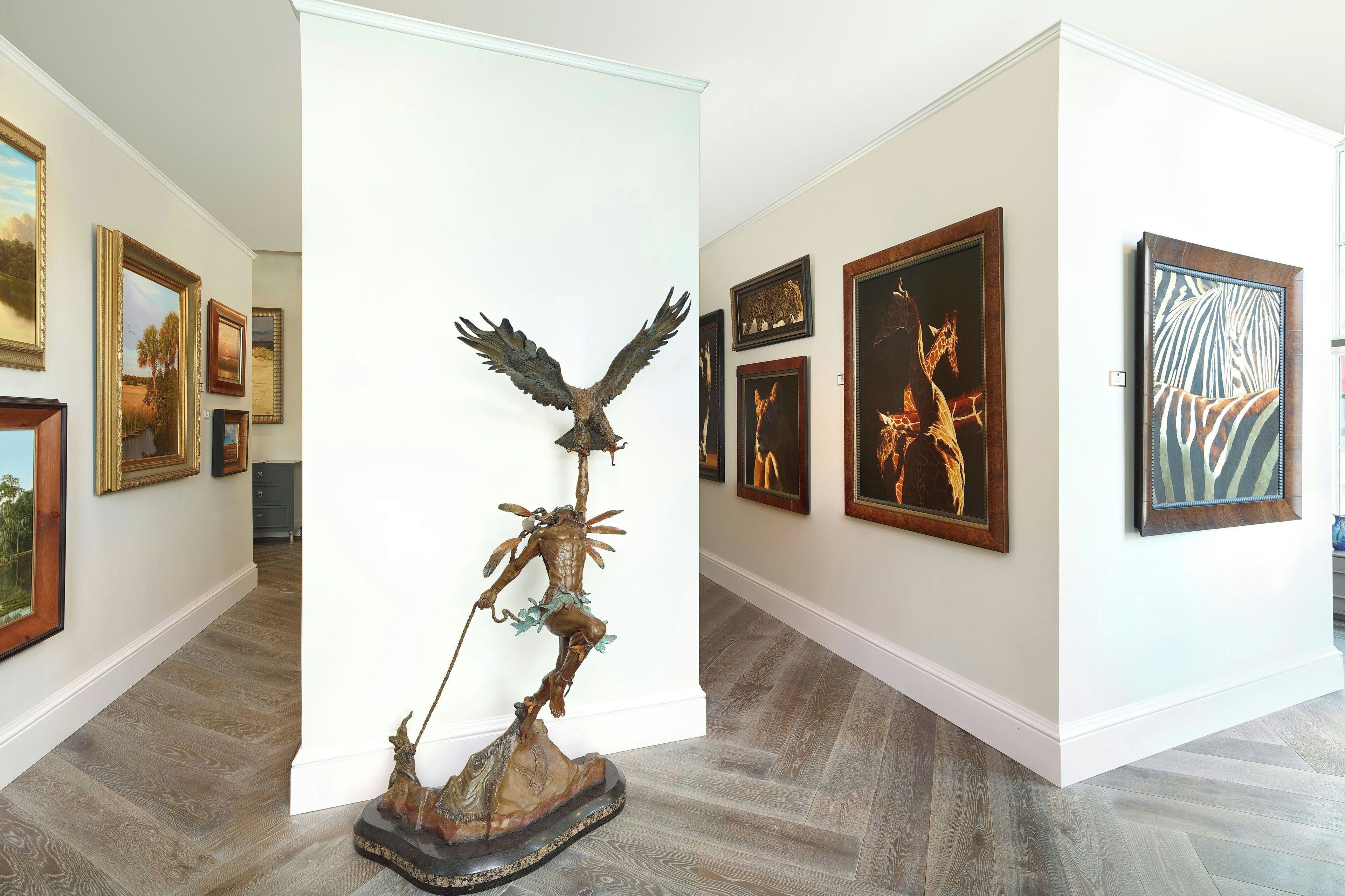 Eine Kunstgalerie mit verschiedenen gerahmten Kunstwerken an den Wänden, einer zentralen Skulptur und einem Holzboden.