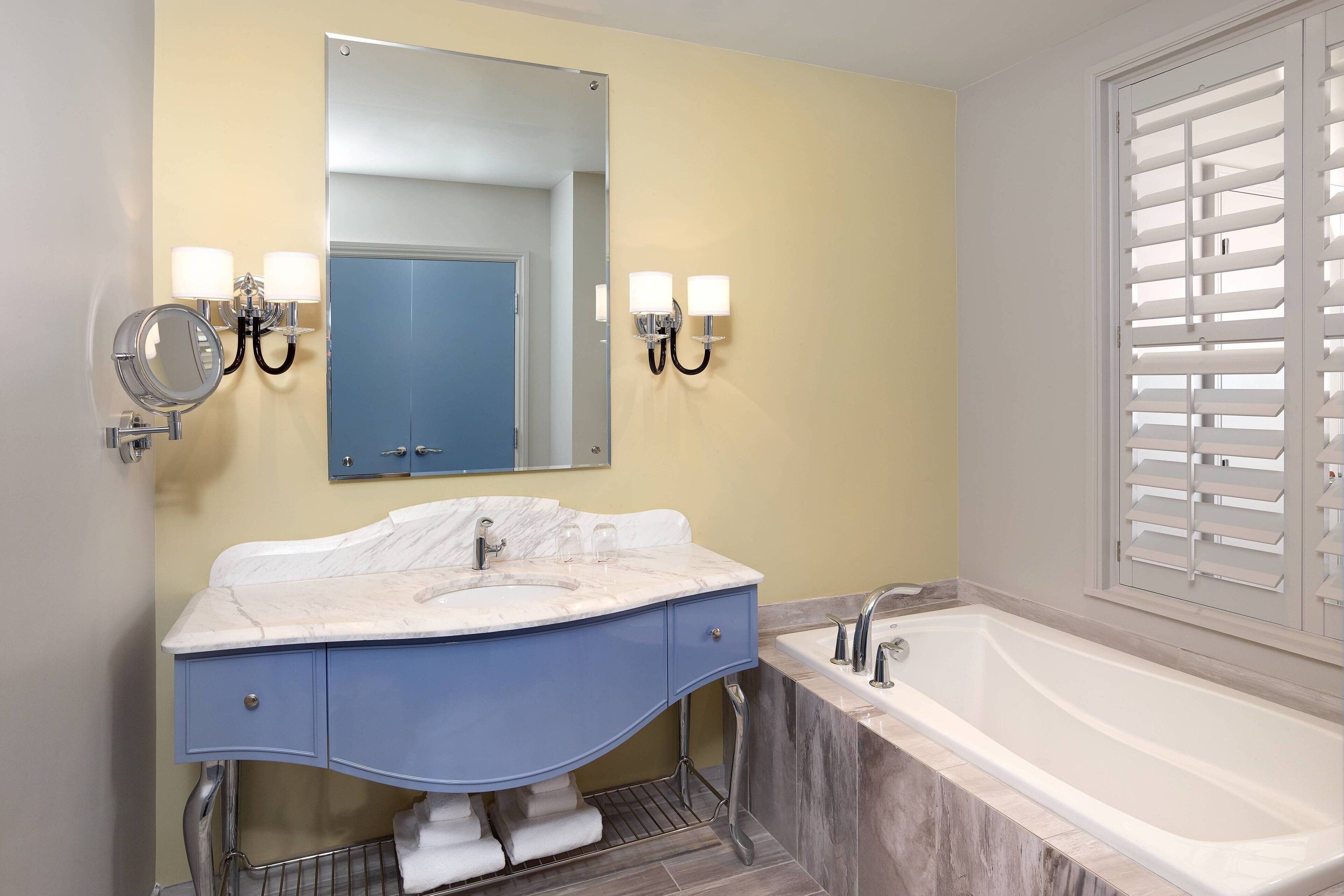 A bathroom with a double sink, a large mirror, wall sconces, and a bathtub.