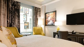 Una habitación de hotel con una cama grande, un escritorio con lámpara, una silla y un televisor en la pared.