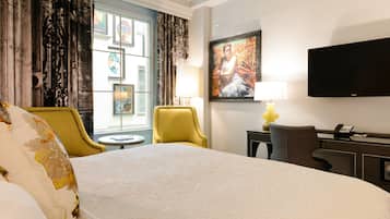 A hotel room with a large bed, a desk with a lamp, a chair, and a television on the wall.