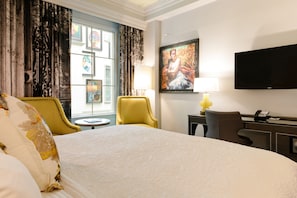 Una habitación de hotel con una cama grande, un escritorio con lámpara, una silla y un televisor en la pared.