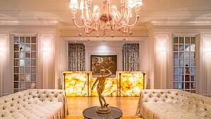 A luxurious lobby with a grand chandelier, a marble reception desk, and two tufted sofas.