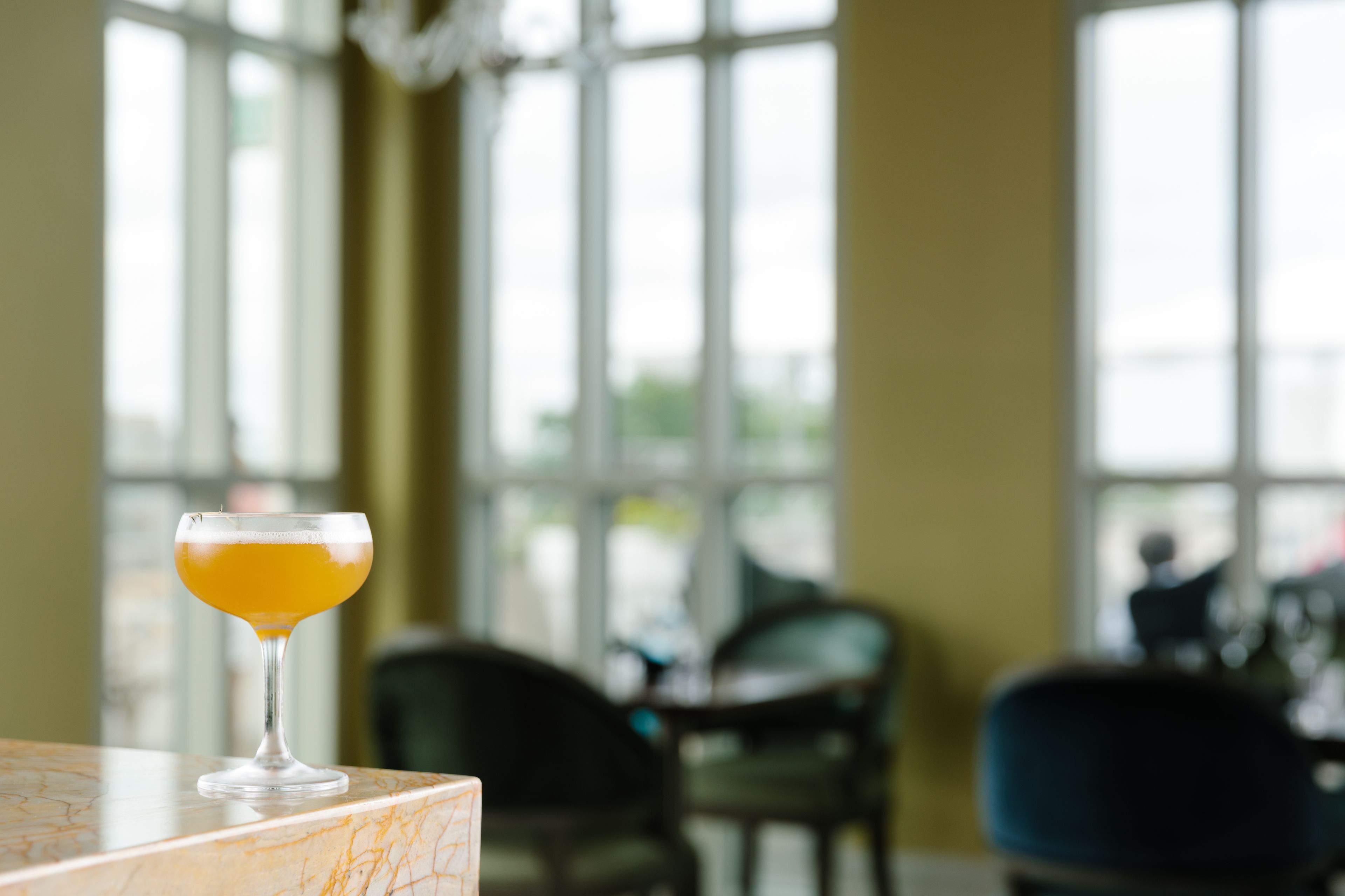 A cocktail glass on a marble surface with large windows in the background.