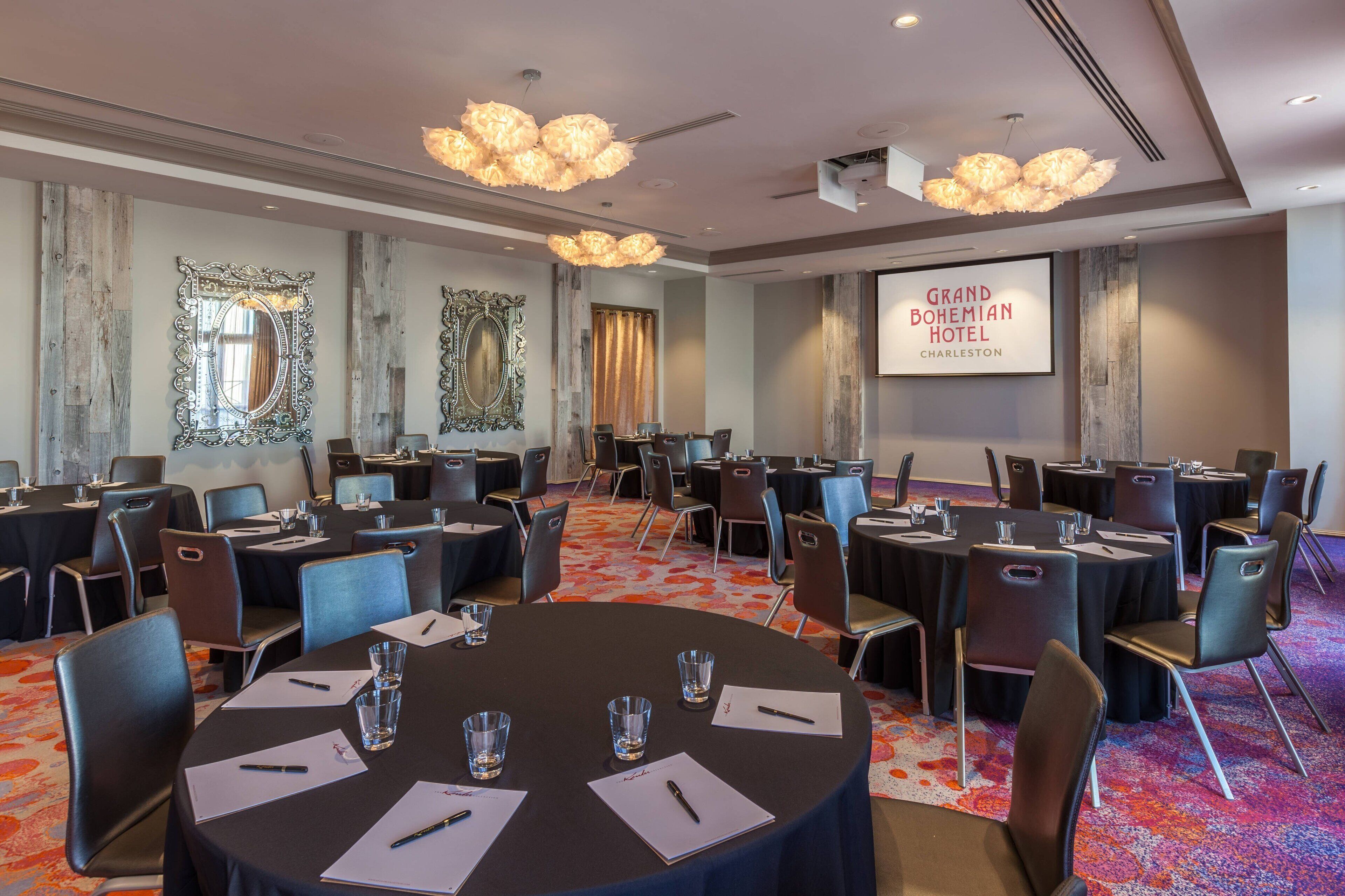 Une salle de conférence équipée de tables rondes, de chaises et d’un grand écran affichant le nom de l’hôtel.